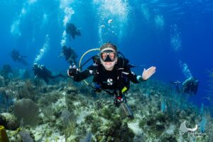 Diver waving at the camera above a coral reef with a group of divers behind, Little Cayman