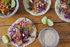 Crispy lionfish tacos topped with red cabbage and salsa, served with lime wedges and a dipping sauce