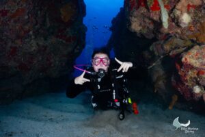Smiling diver in a pink mask posing in a coral swim-through in Little Cayman