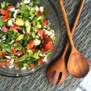 Bowl of lionfish ceviche with tomato, avocado, red onion and coriander, next to wooden salad servers