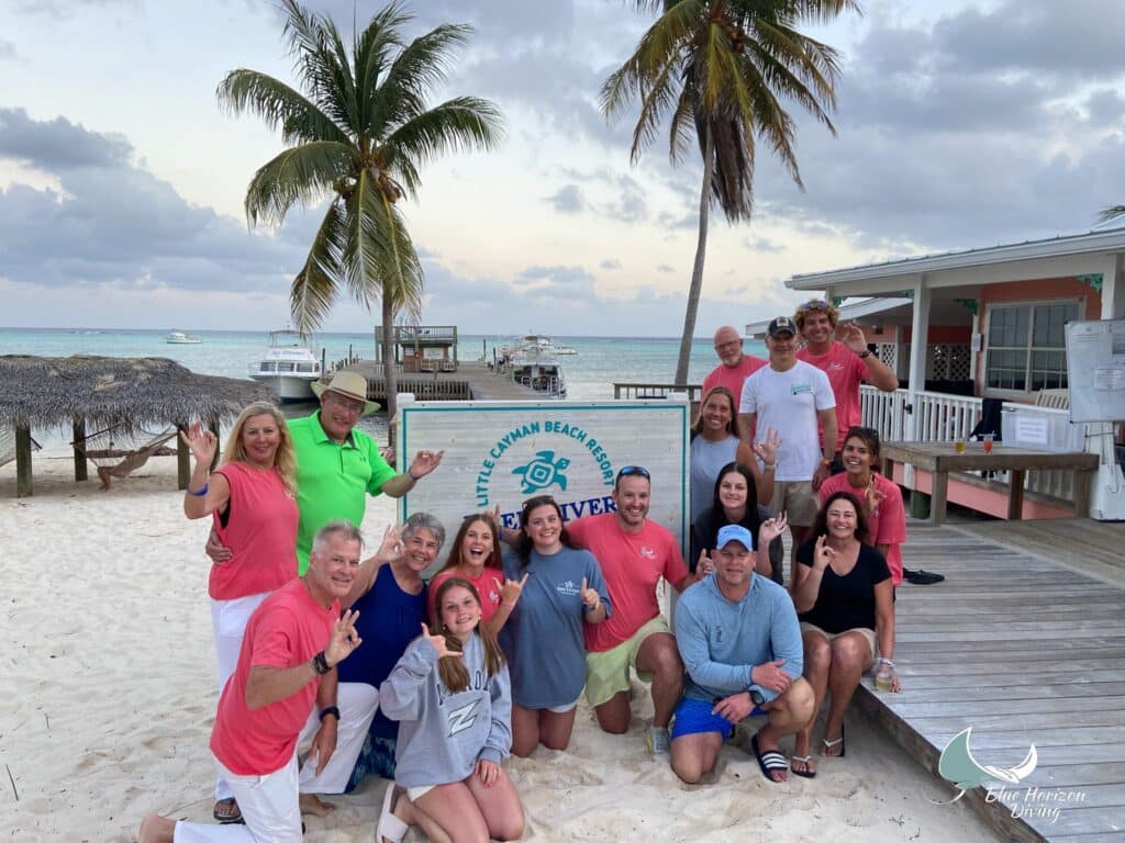 Blue Horizon Diving group posing on the beach by the Little Cayman Beach Resort sign and dive dock