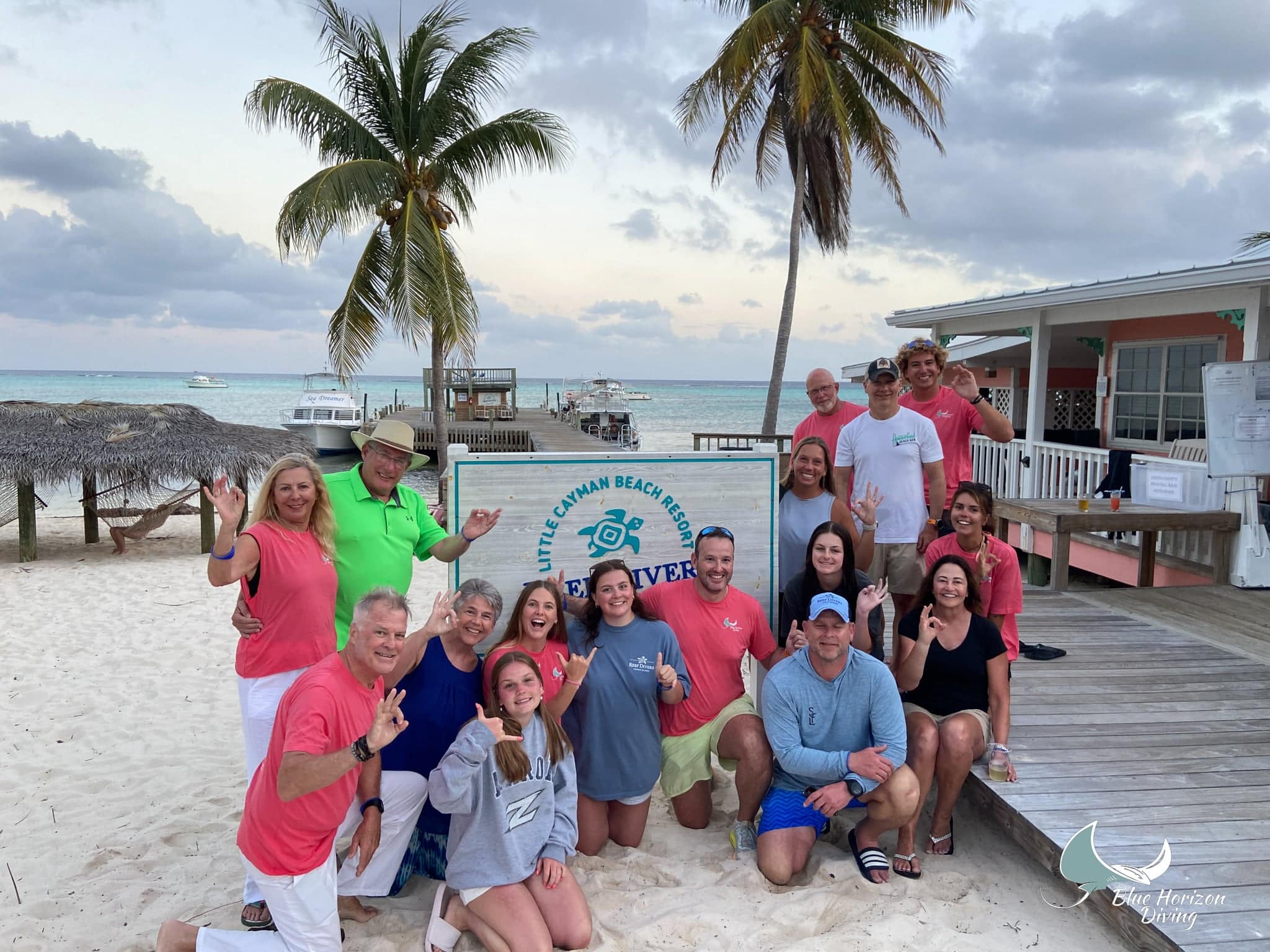 Blue Horizon Diving group posing on the beach by the Little Cayman Beach Resort sign and dive dock